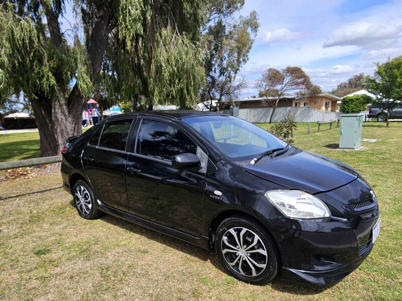 Black Toyota Yaris sedan parked under a tree